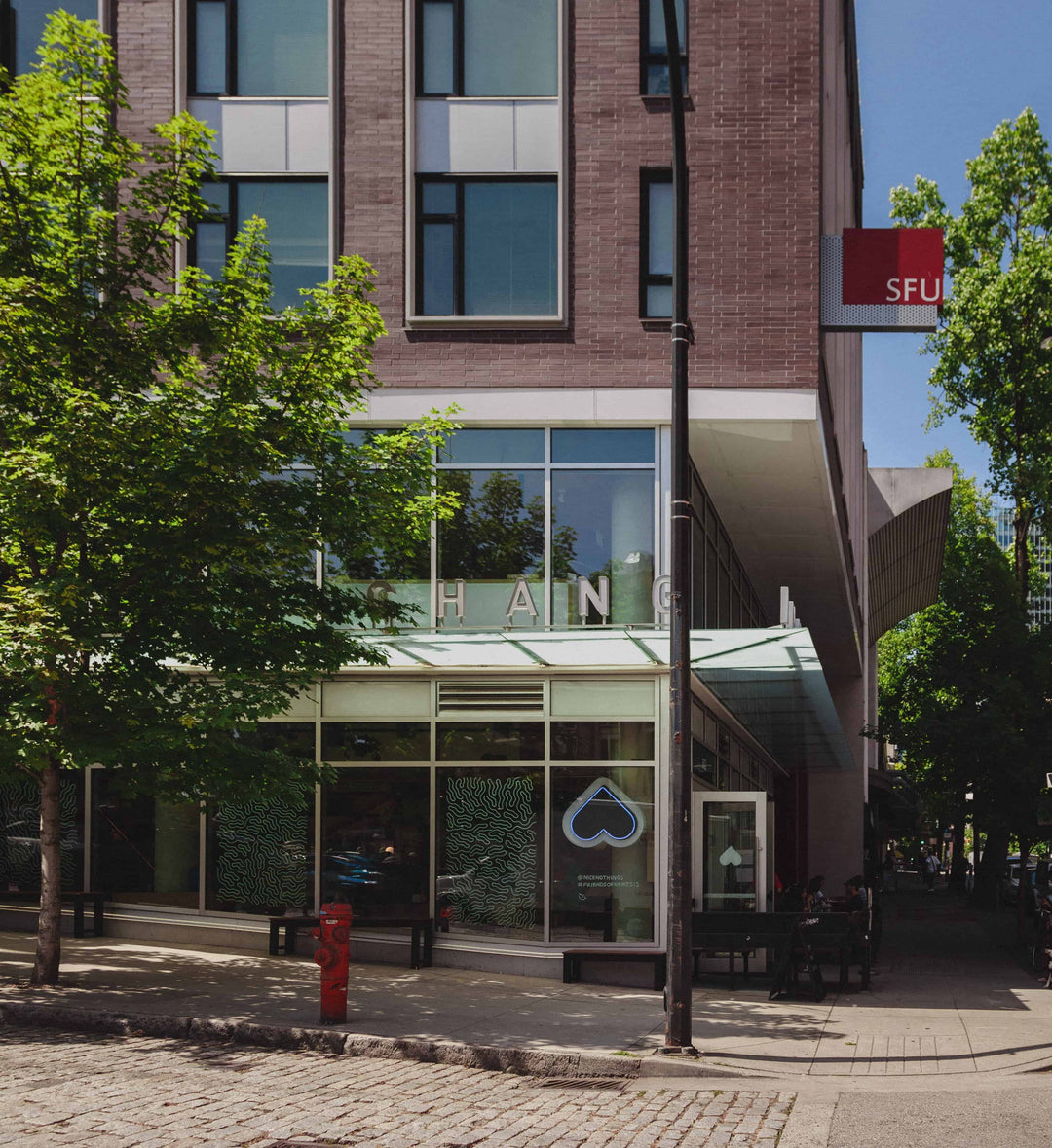 Gastown Nemesis Coffee Shop Location with glass windows, heart logo, brick building and trees on a street corner